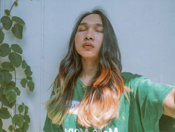 Portrait of young woman standing against wall