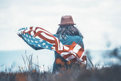 Rear view of man sitting on field against sky