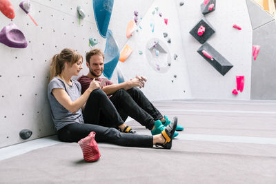 Female showing mobile phone to smiling male friend while sitting in gym