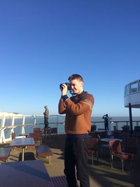 Man photographing in ferry using camera against clear blue sky