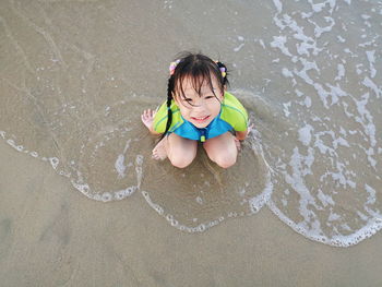 High angle portrait of girl smiling while sitting on shore at beach