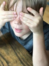 High angle view of playful boy covering his eyes at home