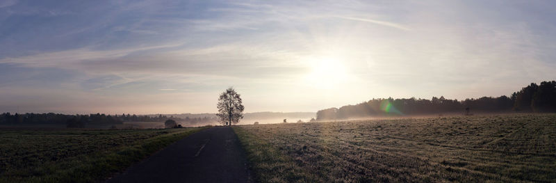 Panoramic shot of empty road amidst field against sky during sunset