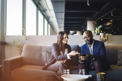 Businessman showing smart phone to businesswoman while sitting in office