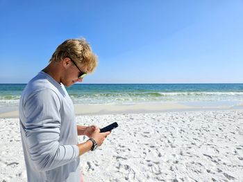 Cute millennial dude texting on beach in summertime.