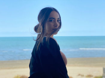 Attractive teenage girl standing at beach against sky