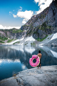 Rear view of man standing on rock by lake against sky