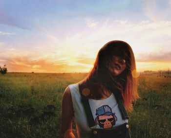 Woman standing on field against sky during sunset