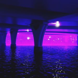 Illuminated bridge over sea against sky at night