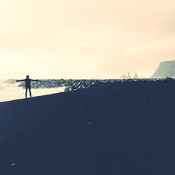 Silhouette woman walking on beach against sky during sunset