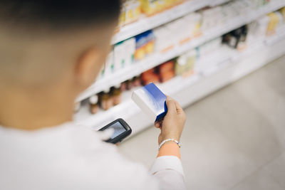 High angle view of male pharmacist using bar code reader on medicine at store