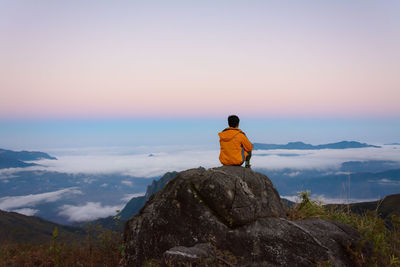 Rear view of man sitting on rock against sky