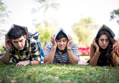 Tired friends with books while lying down on field at park
