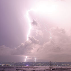 Lightning over illuminated cityscape against sky