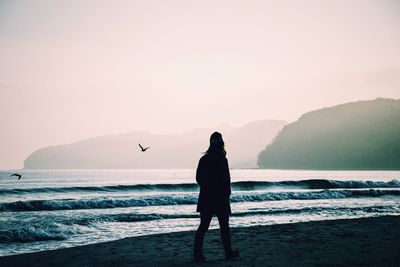 Silhouette woman walking on beach against clear sky