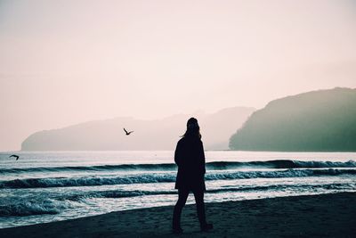 Silhouette man standing on beach against clear sky