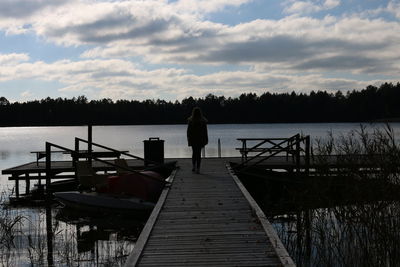 Rear view of pier on lake against cloudy sky
