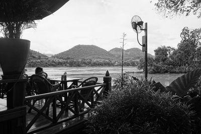 People sitting on riverbank by river against sky