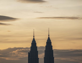 High section of petronas towers against cloudy sky during sunset