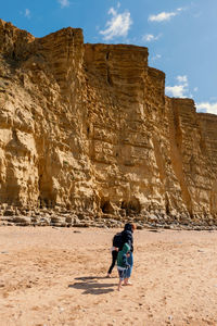 Full length of mother and kids walking on beach against rock formation