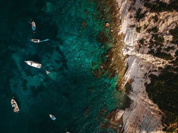 Breathtaking drone view of modern motor boats floating on calm surface of clean turquoise sea near rocky coastline