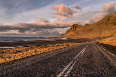 Road leading towards sea against sky during sunset