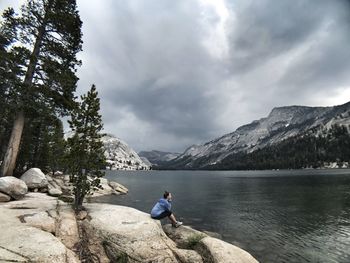 Man on rock by lake against sky