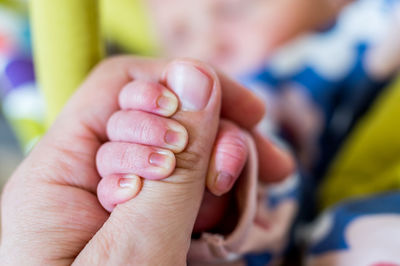 Cropped hand of baby holding mother thumb at home