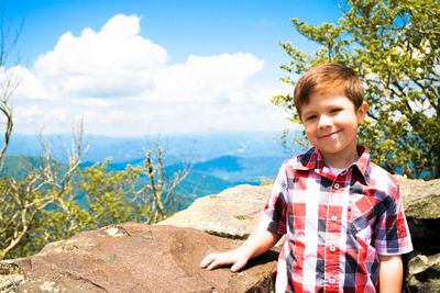 Portrait of smiling boy standing by tree against sky