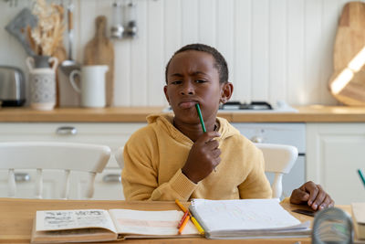 Thoughtful small boy look at camera with pencil near lips think about school study idea sits at home