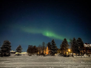 Snow covered landscape against sky with shining aurora borealis at night