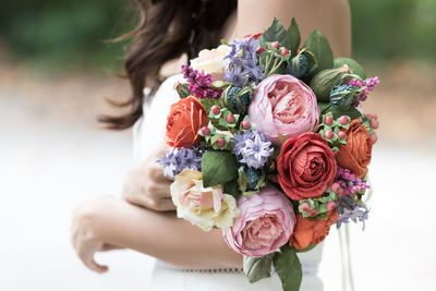 Midsection of bride holding bouquet while standing outdoors