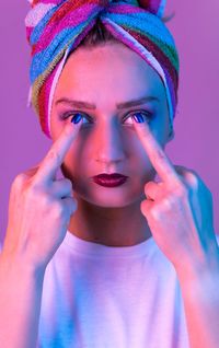 Close-up portrait of young woman showing middle finger over pink background