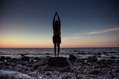 Full length of man exercising at beach against sky during sunset