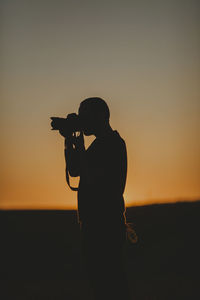 Side view of silhouette photographer against sky during sunset