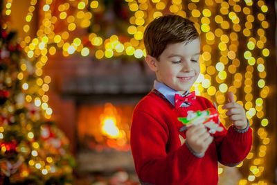 Cute boy holding toy against illuminated christmas light