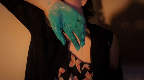 Midsection of woman holding green paint while standing against wall