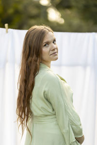 Caucasian pregnant woman hanging up laundry on clothes line outside, drying bed linens, bedding