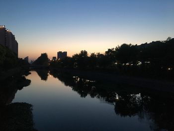 Reflection of silhouette trees and river against sky during sunset