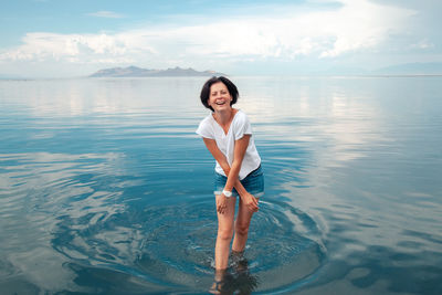 Young woman in denim shorts and white t-shirt enjoying blue lake water and beautiful cloudy sky.