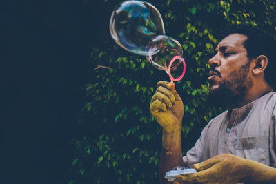 Man blowing bubbles by trees