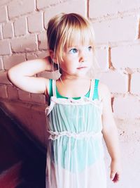 Thoughtful girl standing against brick wall