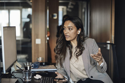 Female entrepreneur looking at computer while talking on smart phone at office