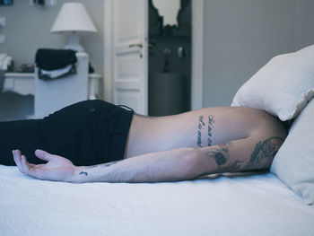 Side view of shirtless man covering head with pillows while lying on bed