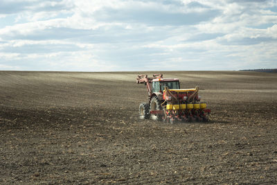 Tractor fertilizing the plowed field, clouds and sky