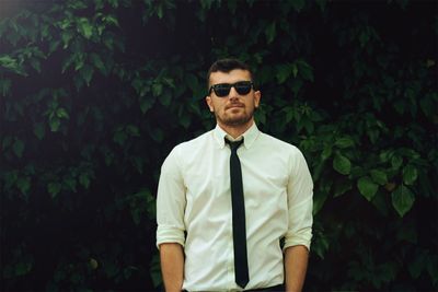 Portrait of young man wearing sunglasses standing against plants