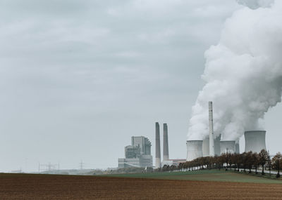 Smoke emitting from factory against sky