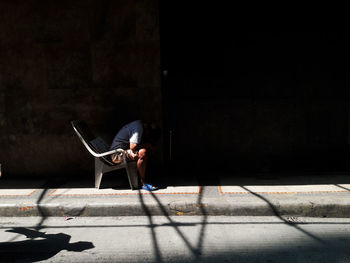 Full length of man relaxing on street against wall
