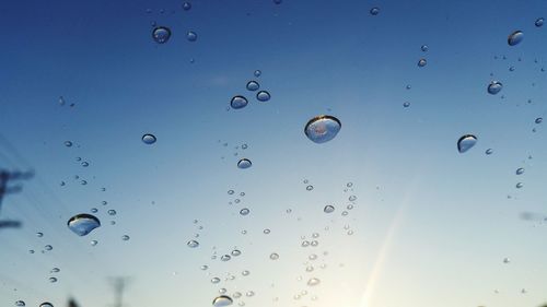 Close-up of water drops on glass against sky