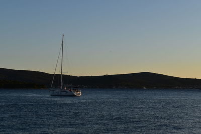 Sailboat sailing on sea against clear sky during sunset